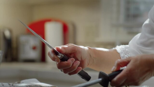 Closeup shot of an Asian woman sharpening a knife