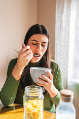 A young woman eating corn flakes for breakfast in the morning in her apartment	