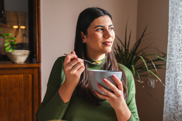 A young woman eating corn flakes for breakfast in the morning in her apartment	