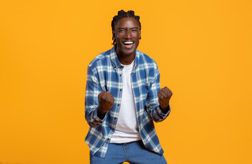 Cheerful young black guy celebrating success on yellow studio background