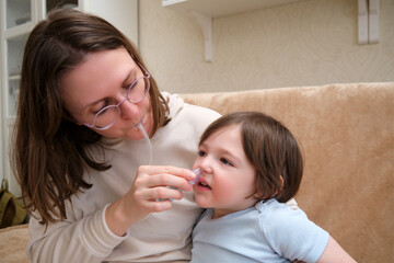 Woman mother using an aspirator to clear snot from baby's nose