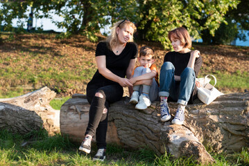 Naklejka na ściany i meble Mother with two children sitting on big tree by river and resting, daughter criticize her little brother and mother calms them both, family relationship, between brother and sister