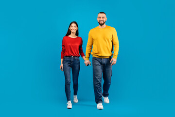 Portrait of happy young caucasian couple holding hands and walking towards camera