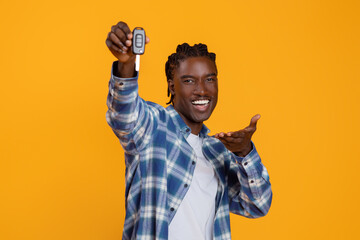 Ecstatic young black man presenting car keys with an outstretched hand - obrazy, fototapety, plakaty