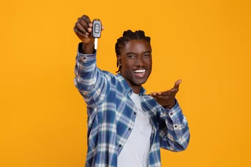 Fototapete Ecstatic young black man presenting car keys with an outstretched hand © Prostock-studio