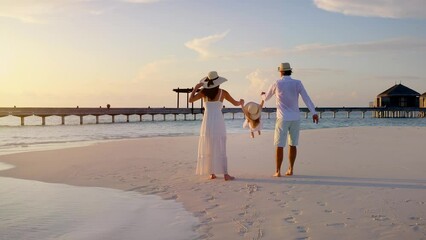 A happy family in white summer clothing is having fun on a tropical beach during sunset time