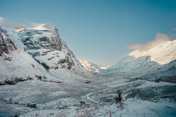 A path winds through a snow-covered landscape with the Three Sisters mountains rising up on the...