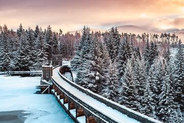 The Laggan Dam (Roybridge Reservoir) and spillway frozen over and covered in snow at sunset