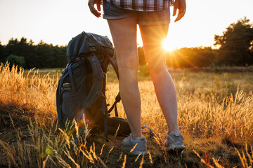 Woman hiker with backpack standing in meadow during sunset. Relaxation during trekking in summer...