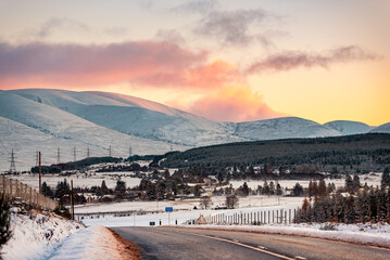 The village of Dalwhinnie in Scotland, against the background of snow-capped mountains under a pink sunset