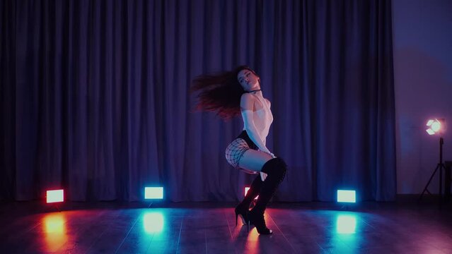 Sexy woman dancing high heels. A dancer girl dances erotically in a dark hall. Twerk, high heels, striptease, a seductive dance. Atmospheric colored light, club, stage.