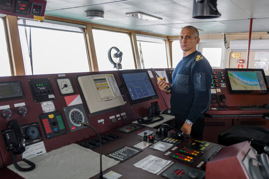 Officer on watch with radio on the navigational bridge. Caucasian man in blue uniform sweater on the bridge of cargo ship.