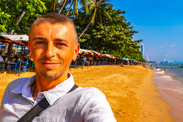 Tourist takes selfie beach waves sand people palm Pattaya Thailand.
