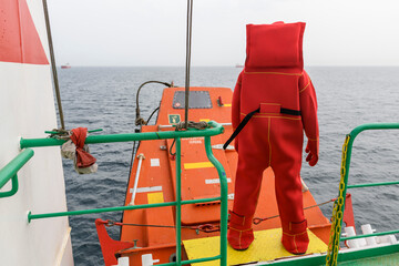 Seaman wearing Immersion Suit on Muster station. Abandon ship drill. Free fall boat. Cargo vessel.