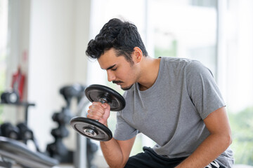 Young man concentrating on bicep curls with a dumbbell at the gym