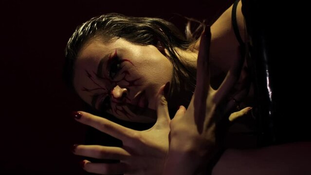 Dancing in the dark, a beautiful girl on a black background. Dance choreography of a young woman, she is dressed in black clothes. Sexy scene, she has weird makeup on her face. Great flexibility