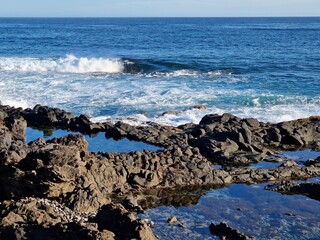 Rocky shore and natural pools of Tenerife coast, with white rolling waves of the sea breaking