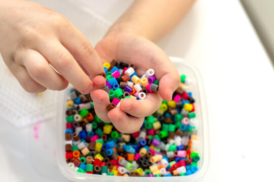 Close-up of a lot of perler beads in children's hands, the child chooses a piece of a colored mosaic