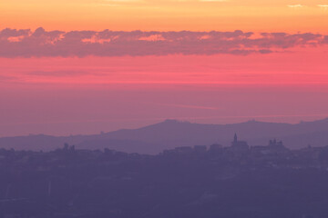 pink sunrise sky with the silhouette of an italian village on the top of a hill in Piedmont