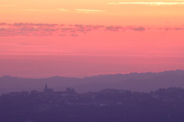 pink sunrise sky with the silhouette of an italian village on the top of a hill in Piedmont