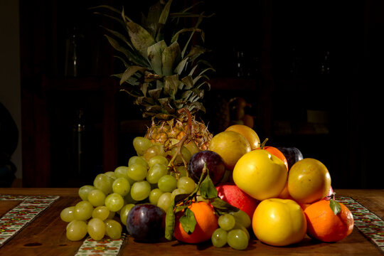 Close-up of a stack of grapes, apples, satsumas, plums and a pineapple on a table