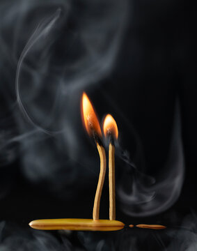 Close-up of two burning matchsticks and smoke against a black background