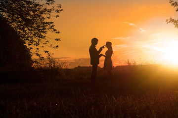 Silhouette of a couple standing in a wheat field at sunset with the man touching the woman's nose, Hungary