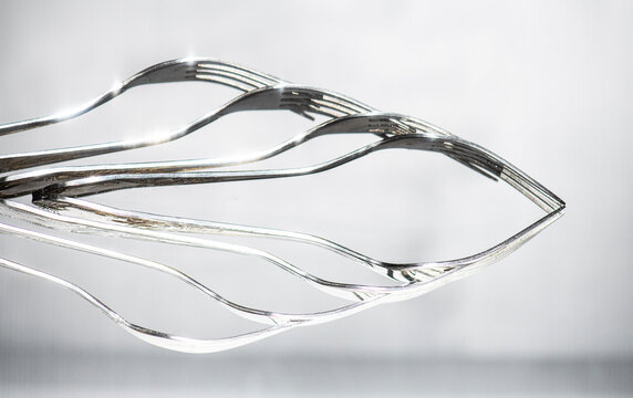 Abstract reflection of four silver forks against a grey background
