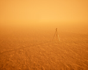Land surveyor on tripod standing on wide open flat landscape in mist during sunset. - 745287929