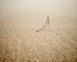 Land surveyor on tripod standing on wide open flat landscape in mist. High angle view.