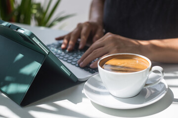 Woman drinking strong coffee in the morning and working on tab computer. A young female designer works in a cafe. Concept of working remotely.