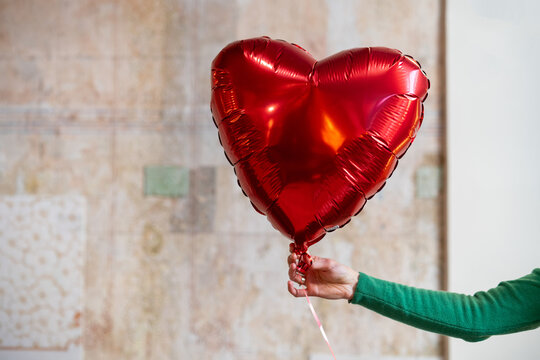 Close-up of a woman's hand holding a red heart shaped balloon
