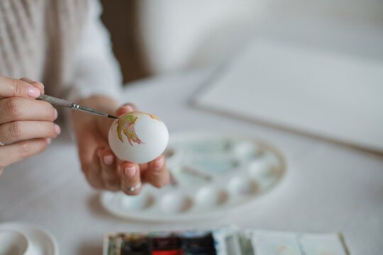 Close-up of a woman sitting at a dining table decorating an Easter Egg