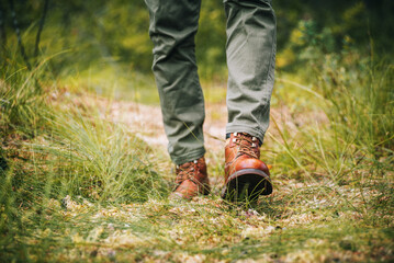 A man walking along a forest path. Brown boots in close-up. Hiking in autumn forest.
