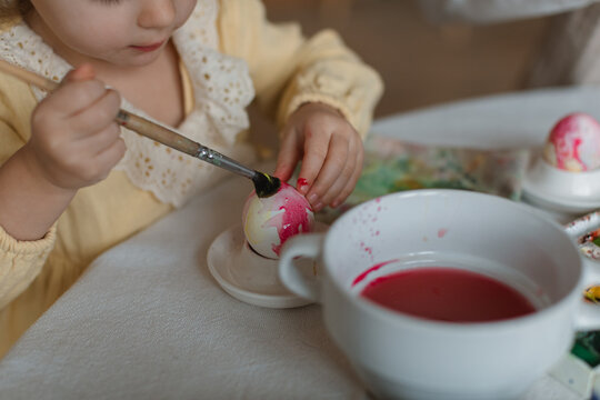 Close-up of a toddler sitting at a dining table decorating an Easter Egg