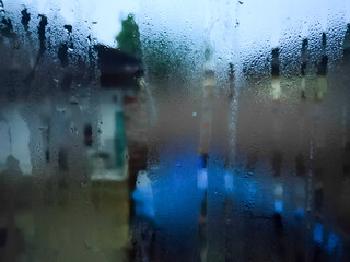 Rainwater flows down the window pane creating a blurry outside reflection.  suitable for backgrounds, presentations and social media.