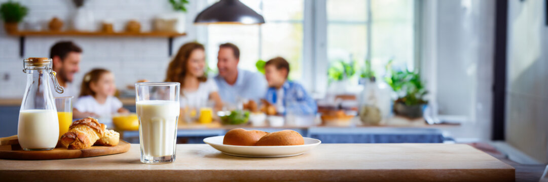 Happy family having breakfast at home. Focus on the glass of milk, panoramic image with copy space