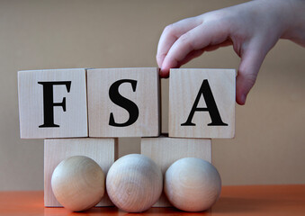 A child's hand places a large cube next to other cubes. FSA acronym concept