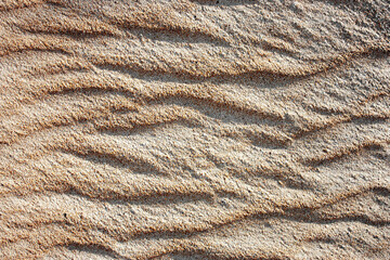 Waves on the surface of the sand, top view. The wavy surface of coastal sand. The structure of waves on sea sand.