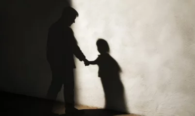 Fotobehang Disturbing image depicting the silhouette of an adult man holding hands with a child, symbolizing the dark realities of child trafficking, theft, and abuse © giedriius