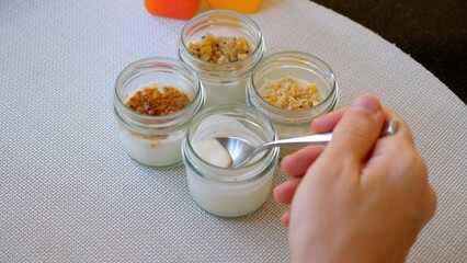 Person preparing homemade yogurt with various toppings, arranged for display on kitchen counter. Tasty and nutritious homemade breakfast.