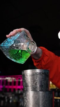 The bartender's hand pours green absinthe from a clear bottle into a shaker vertical video