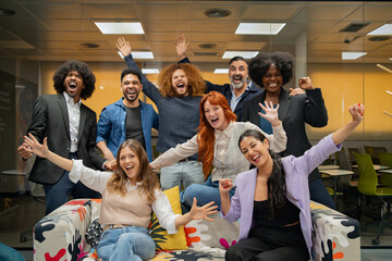 Diverse office team jubilantly raises hands in celebration, showing teamwork and happiness at work. 