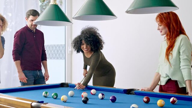 Two couples at a billiards table, with one woman grinning despite not pocketing the ball, in a well-lit room. 