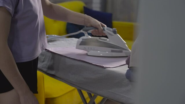 Modern woman irons clothes at home after washing on an ironing board in the hall. Independent wife who does household chores, housework and hygiene.