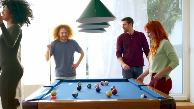 Four friends play pool, with one woman excitedly reacting to sinking a ball, in a room with natural light.  - Powered by Adobe