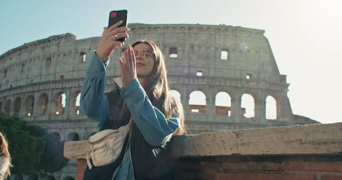 A woman is capturing a selfie with the Colosseum's magnificent facade as a backdrop, enjoying the sky and reflecting her travel adventures in the city of Rome, a perfect moment of tourism.