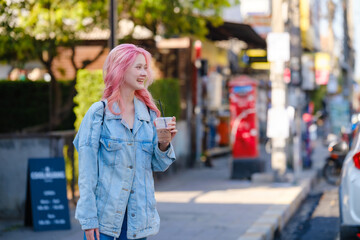 Asian female backpacker waiting for the mass transportation tuk tuk besides the road in the city.