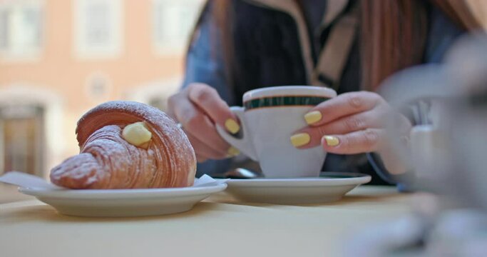 A close-up of the girl takes a cup of coffee with her hands and drinks it. Breakfast in a cafe on the streets of the city with tea and a croissant. High quality 4k footage