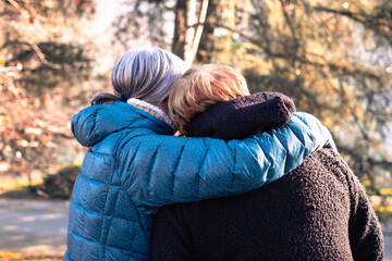 Back view of two elderly women embrace in the park, couple of senior friends or sisters stay together expressing love and support
